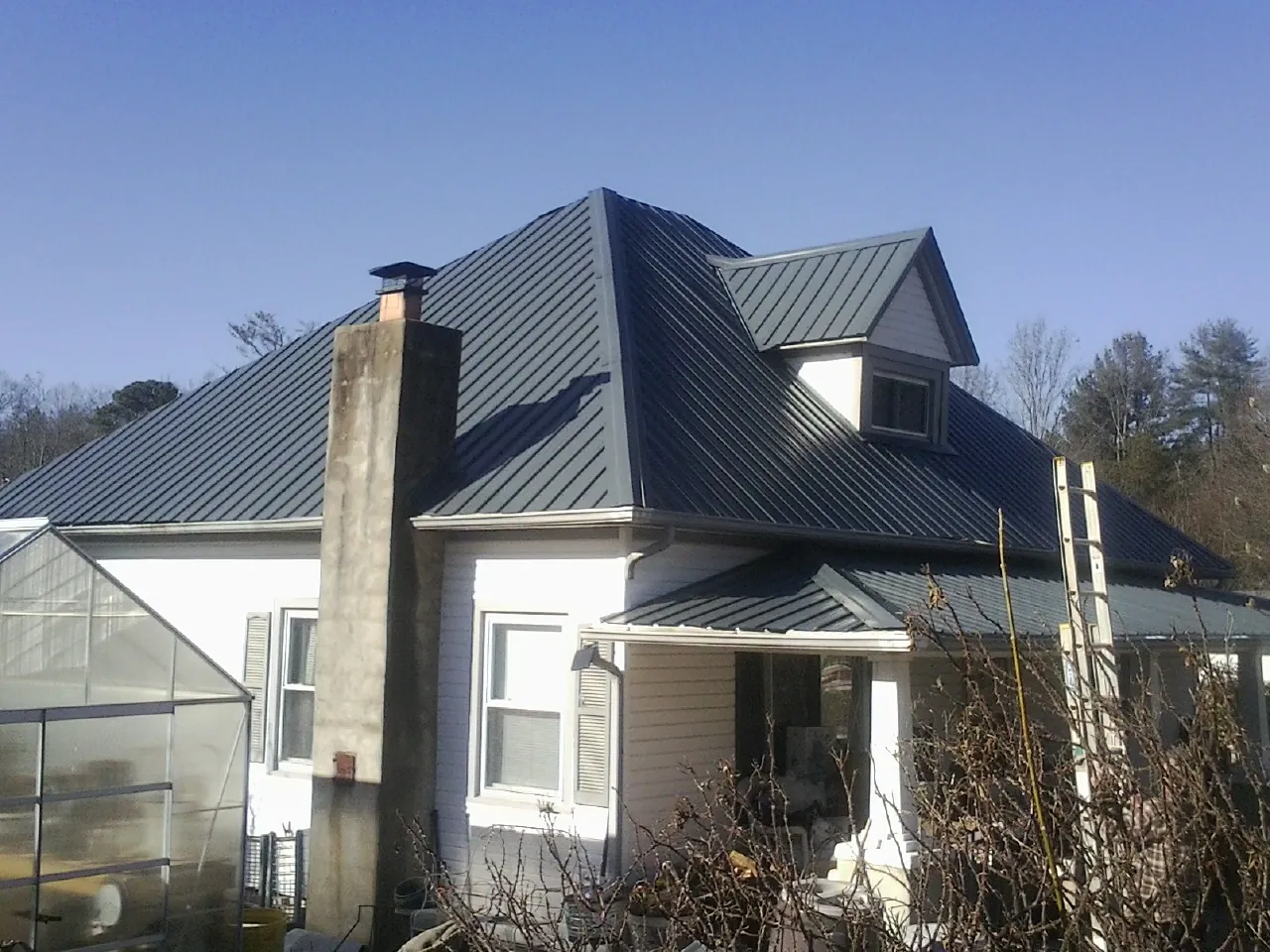Dark blue standing seam metal roof on a white farmhouse with dormer — Slate & Tile Roof Repair by Roofing Brothers in Parrott