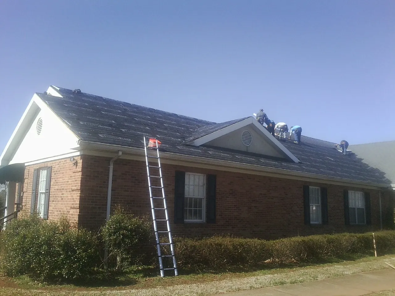 Crew tearing shingles off a brick ranch roof with a ladder set — Emergency Roof Repair work by our crew in Parrott