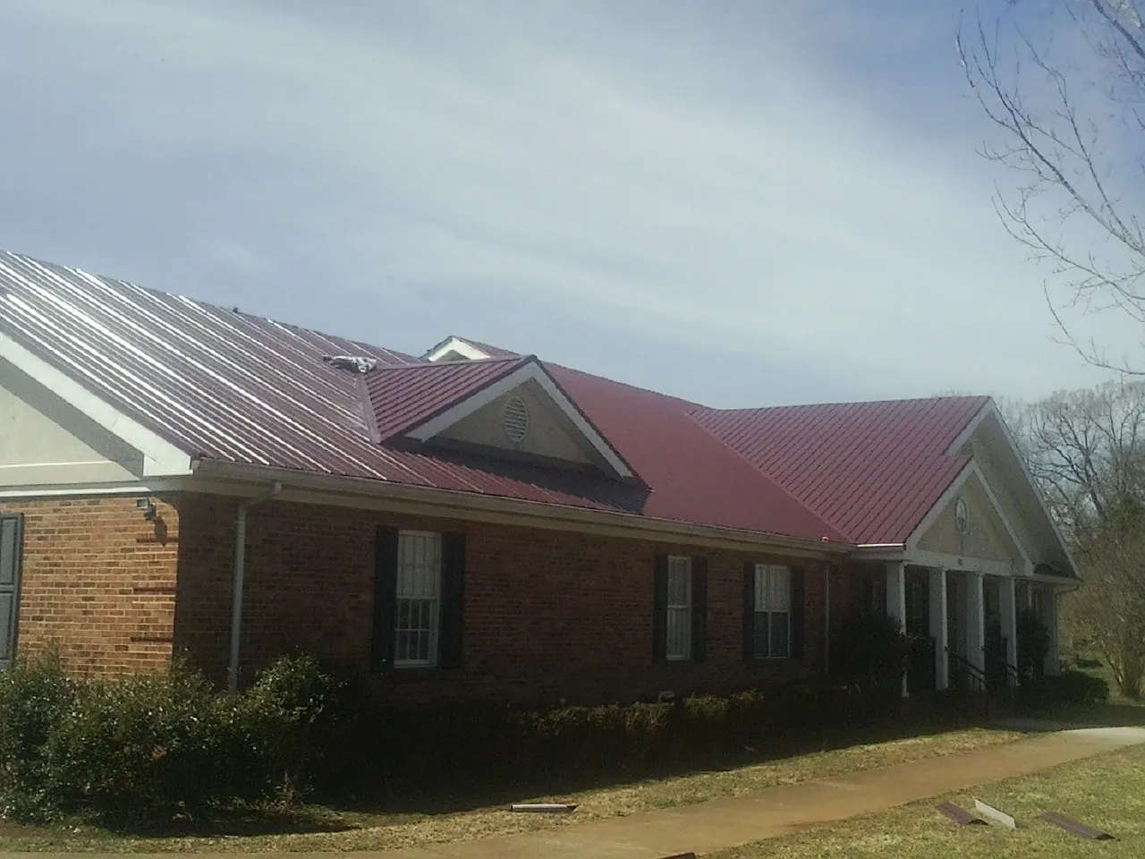 Red metal roof with gabled entries on a long brick building, from a Hail Damage Roof Repair job in Parrott