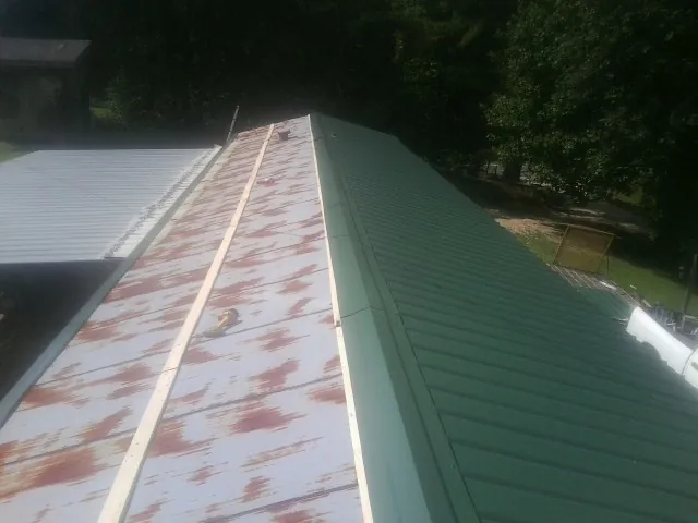 Old rusted panels beside newly installed green metal roofing — Wind Damage Roof Repair by Roofing Brothers in Parrott