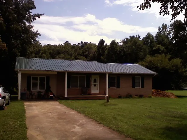 Dark green metal roof on a brick ranch with a covered porch in Parrott