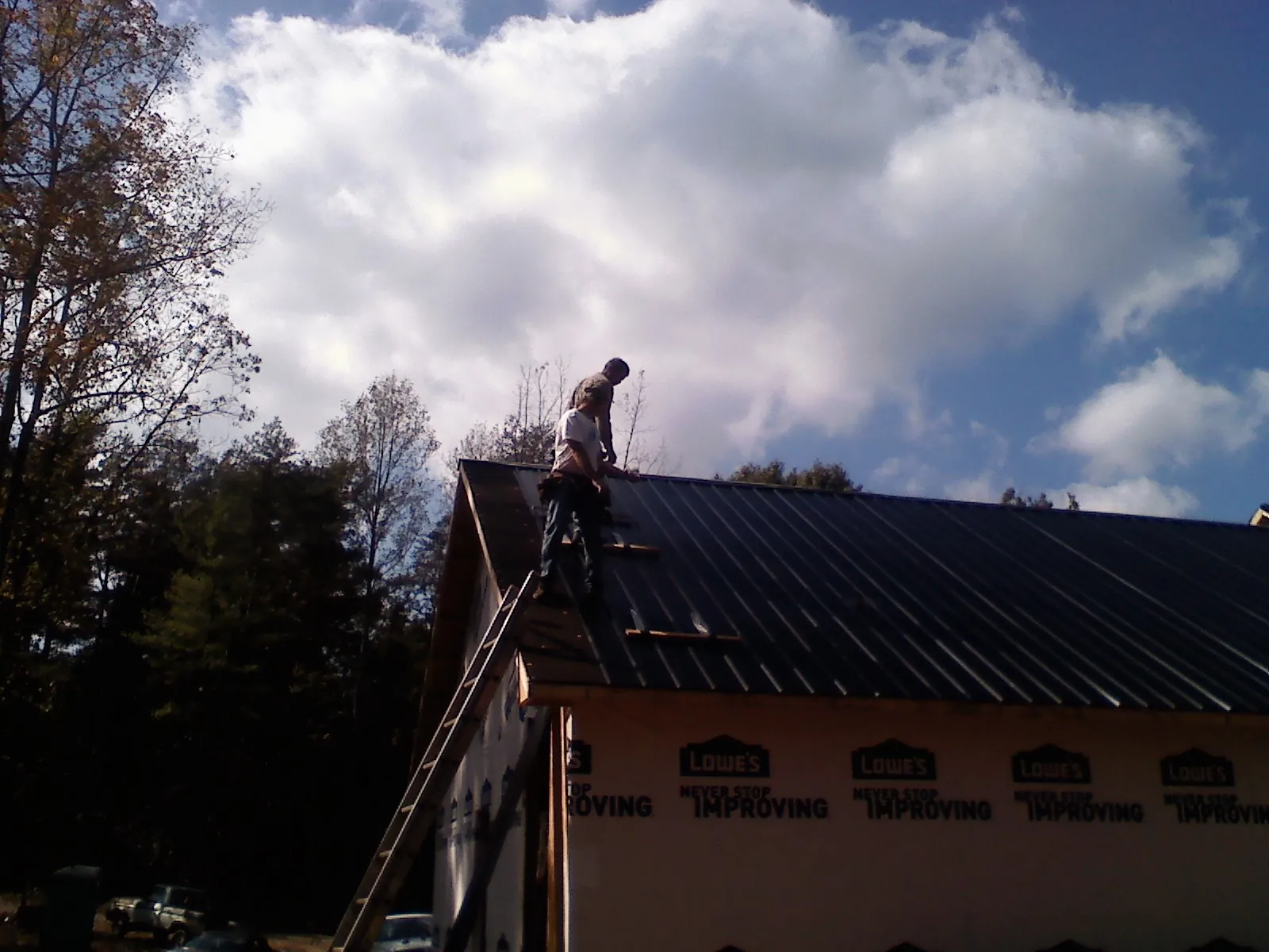 Roofer fastening dark metal panels high against a cloudy sky, from a Roof Inspection job in Parrott