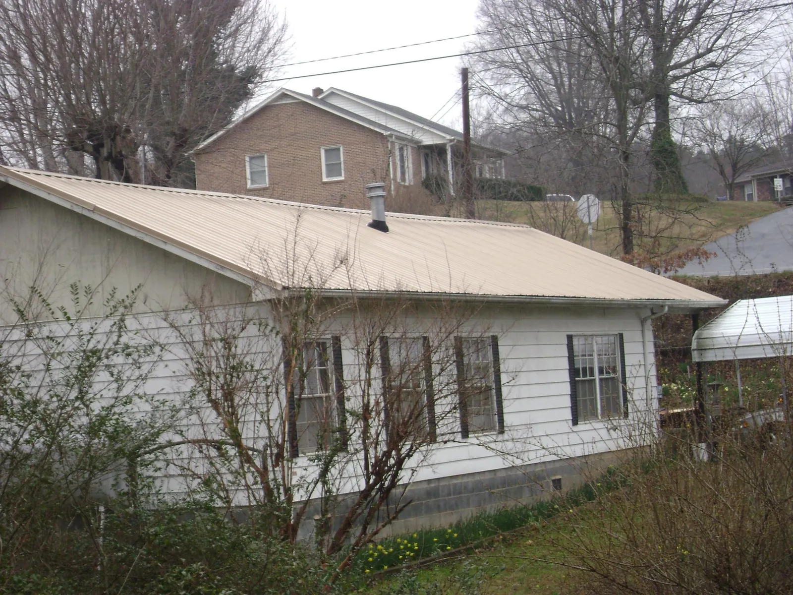 Tan metal roof on a white sided house set into a hillside — Commercial Roofing by Roofing Brothers in Parrott